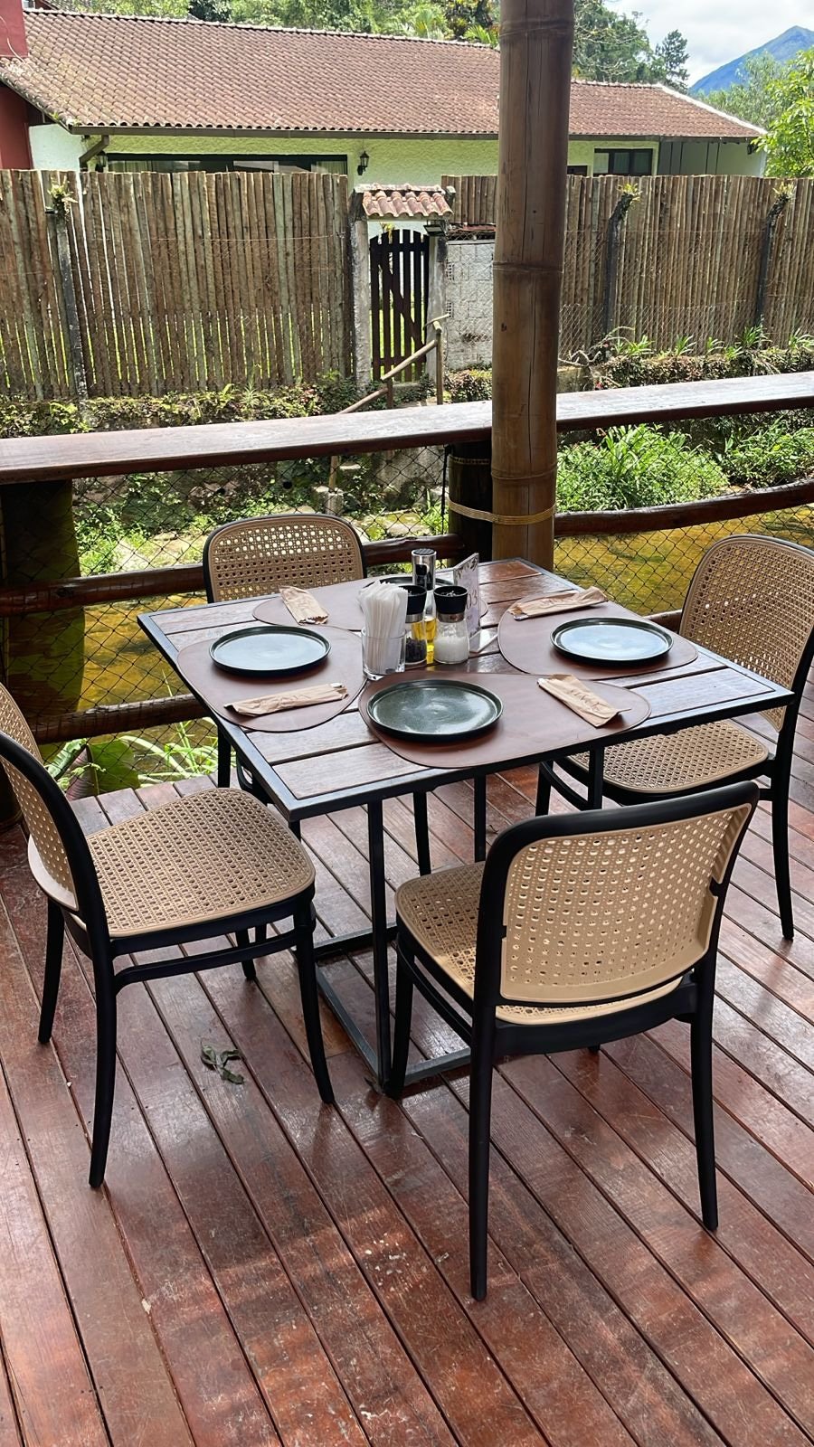 Deck de restaurante com mesa quadrada de madeira e quatro cadeiras Roma pretas com palha sintética em projeto de fit-out