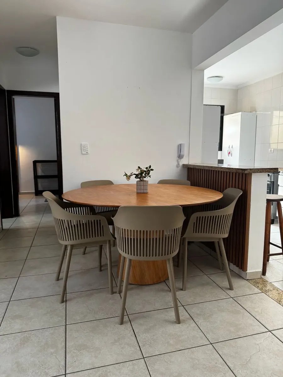 Sala de jantar de apartamento com mesa redonda de madeira e cadeiras Marcela nude com braços integrada à cozinha americana